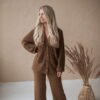 A blond girl wearing wide-leg trousers and a classic English rib cardigan in brown merino wool. Handmade.