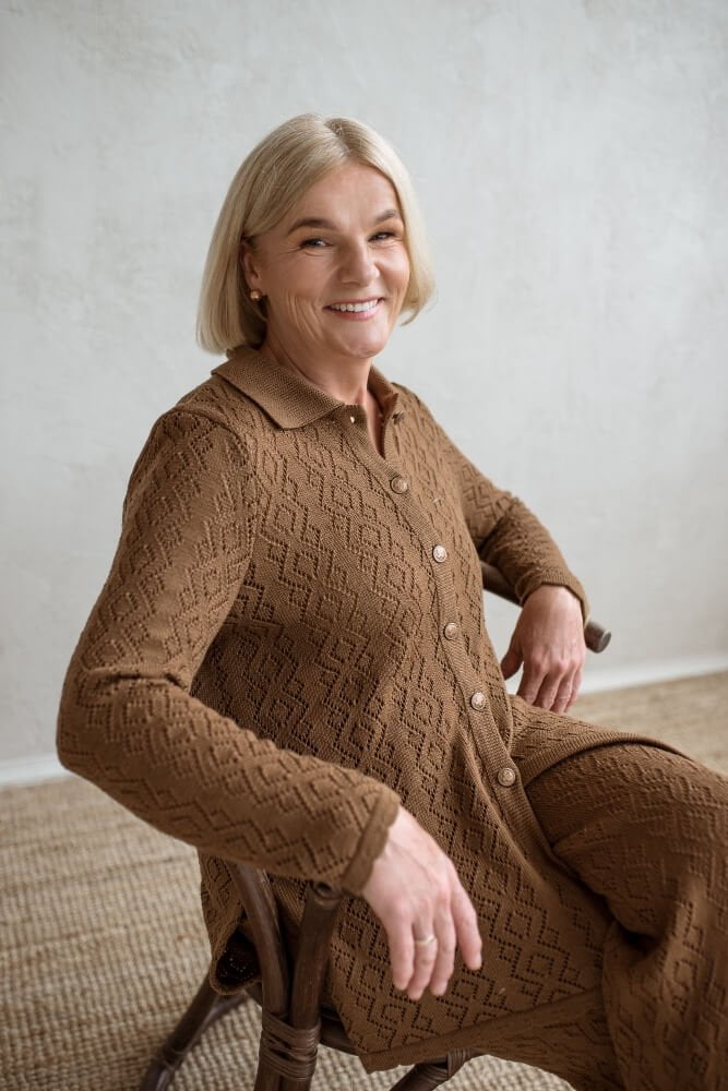 A mid-age lady wearing a brown knit lace set consisting of a button-up shirt-like blouse and matching pattern wide-leg pants